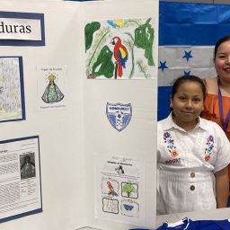 Altair Magaña, alumna de cuarto grado posa junto a su mamá, Ingrid Cruz, junto a la mesa dedicada a la cultura hondureña, el 9 de febrero en el gimnasio de la Academia SPSA.