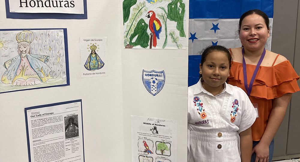 Altair Magaña, alumna de cuarto grado posa junto a su mamá, Ingrid Cruz, junto a la mesa dedicada a la cultura hondureña, el 9 de febrero en el gimnasio de la Academia SPSA.