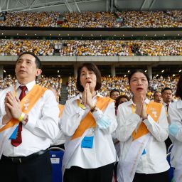 People stand with hands folded in prayer in Singapore's National Stadium during Mass with Pope Francis.