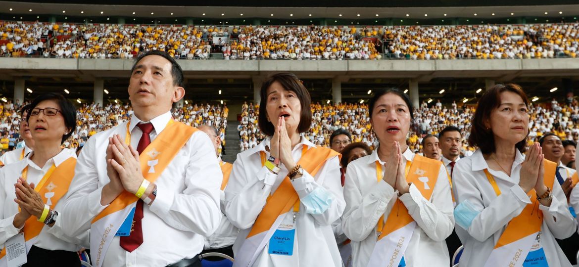 People stand with hands folded in prayer in Singapore's National Stadium during Mass with Pope Francis.