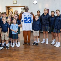 Charles Dupree holds up a Dallas Cowboys jersey while surrounded by St. Monica Catholic School students.