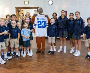 Charles Dupree holds up a Dallas Cowboys jersey while surrounded by St. Monica Catholic School students.