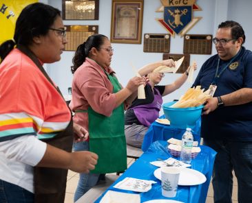 L-R: Teresa Lozano and Evelyn Argueta, receive corn husks from Principal Victor Argueta, right, as a small group of catholics prepare to learn how to make tamales during a class at St. Mary of Carmel Catholic Parish in Dallas, on Dec. 14th, 2024.