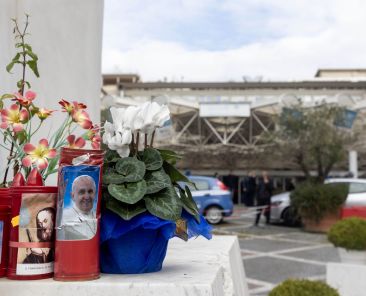 Flowers and votive candles sit at the base of a statue of St. John Paul II outside Rome's Gemelli hospital Feb. 18, 2025, where Pope Francis is a patient. (CNS photo/Pablo Esparza)