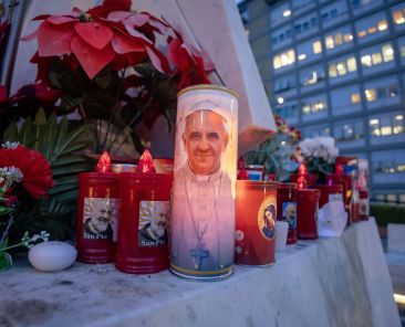 Votive candles and flowers are seen at the base of a statue of St. John Paul II outside Rome's Gemelli hospital Feb. 19, 2025, where Pope Francis is being treated for double pneumonia. (CNS photo/Pablo Esparza)