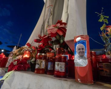 Velas votivas, algunas de ellas con una foto del Papa Francisco, se ven en la base de una estatua de San Juan Pablo II afuera del hospital Gemelli de Roma el 15 de febrero de 2025. (CNS photo/Pablo Esparza)