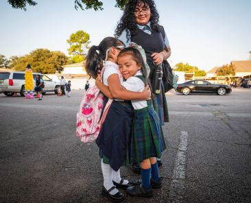 Penelope Medina, left, is hugged by friend Noemi Lujano as Audrey Medina watches, during the first day of classes at St. Mary of Carmel Catholic School in Dallas, on Aug. 8, 2025.