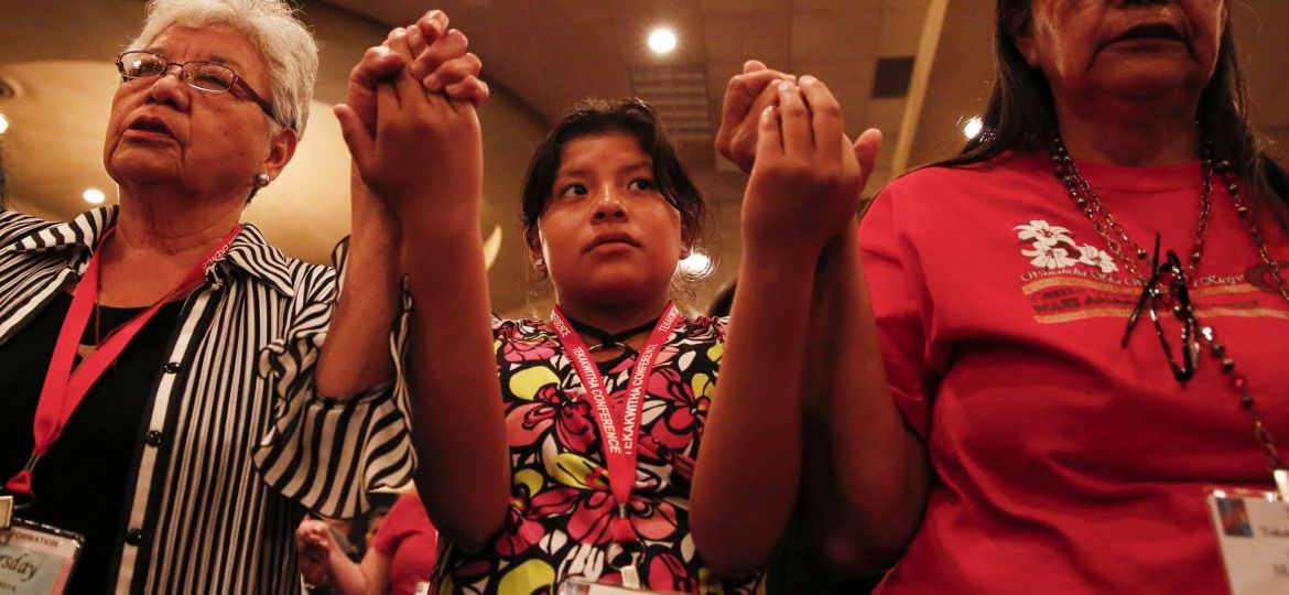 Attendees of Tekakwitha Conference in Fargo hold hands as they pray Our Father during Mass