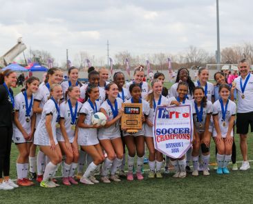 Members of the Bishop Lynch High School women’s soccer team pose with the TAPPS Division I championship banner and trophy after defeating Houston St. Agnes Academy 1-0 in overtime in the state final March 6 in Round Rock. (Bishop Lynch High School photo)