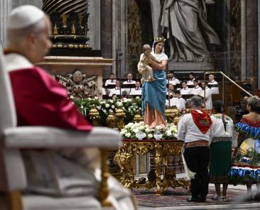 El Papa León XIV observa mientras los fieles --vestidos con atuendos que representan a las naciones del continente americano-- encienden una lámpara bajo una estatua de Nuestra Señora Reina de la Paz en la Basílica de San Pedro, en el Vaticano, el 11 de abril de 2026, durante una vigilia de oración y el rezo del rosario por la paz. (Foto CNS/Vatican Media)