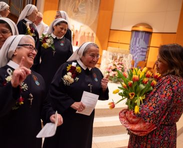 Sr. Norma Edith Munoz, far-left, and Sr. Mickey Espinoza, interact with Maria Rocha, right, St. Monica Director of Faith Formation, after a special Mass honoring the Missionary of the Poor nuns, on April 21, 2026 at St. Monica Catholic parish in Dallas. Mrs. Rocha holds a collection of flowers after being thanked for organizing the special special Mass that celebrated the order’s 100th anniversary.