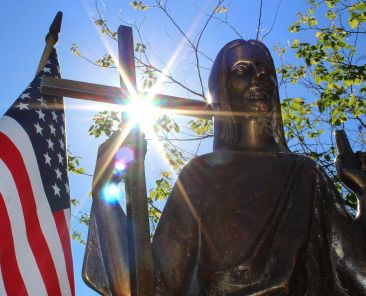 The sun shines through a statue of Christ on a grave marker alongside an American flag at St. Mary Catholic Cemetery in Appleton, Wis., in this 2018 photo. The U.S. Conference of Catholic Bishops' 2026 observance of Religious Freedom Week is June 22-29, and it is more timely than ever, Emily Schumacher-Novak, associate director of education and outreach for the USCCB's Secretariat of Justice and Peace, told OSV News. (OSV News file photo/Bradley Birkholz)