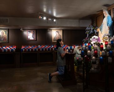 A visitor kneels before a statue of the Blessed Mother at the National Shrine of Our Lady of Champion's Oratory in Champion, Wis., July 1, 2026. Red, white and blue candles were installed in the Oratory as part of the shrine's Catholic Saints of America celebration July 1-9. (OSV News photo/Sam Lucero)